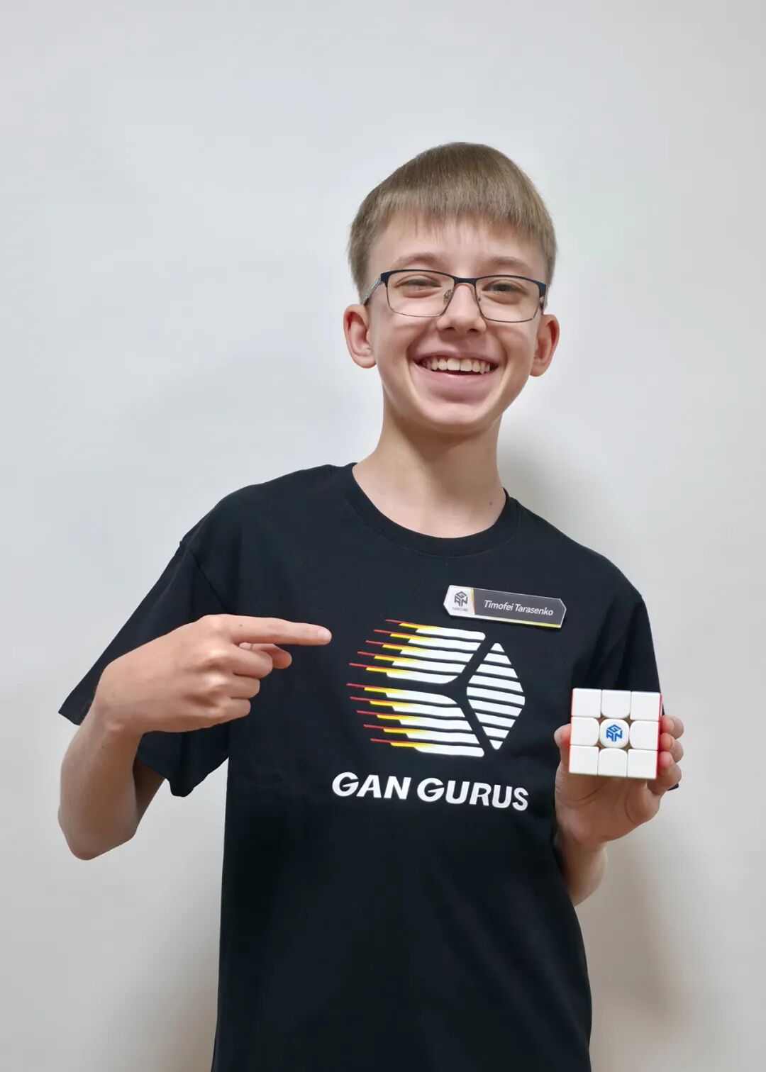Timofei pointing at the logo while holding a GAN speed cube