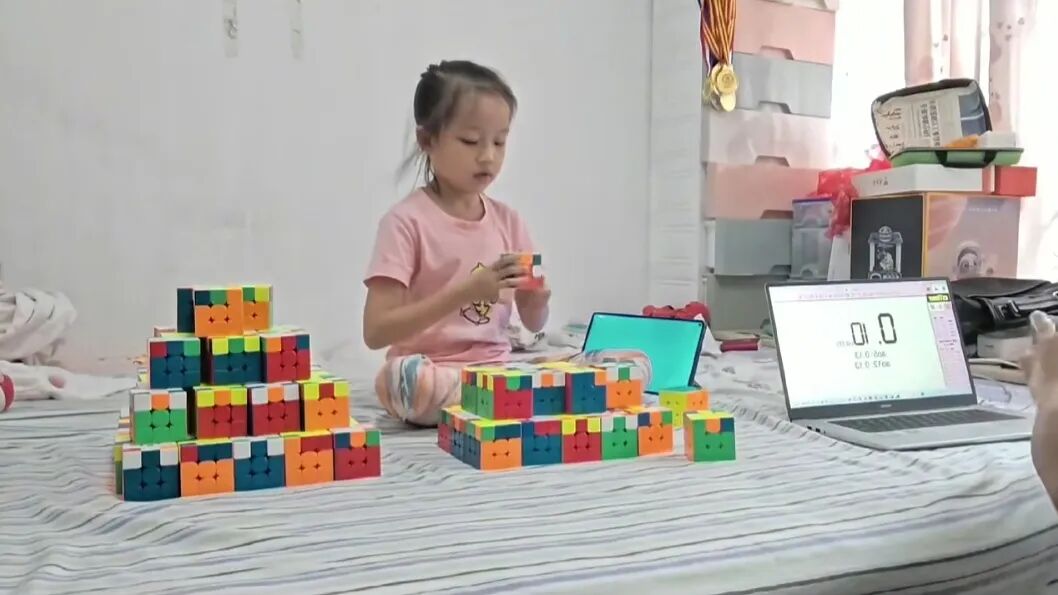 Deng Wanying practicing speed cube drills at home with multiple cubes and a competition timer setup