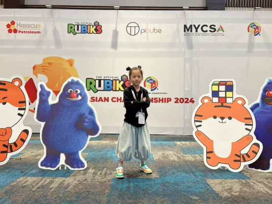 Child poses at Rubik's Cube Asian Championship 2024 with cartoon tiger and blue mascot cutouts.